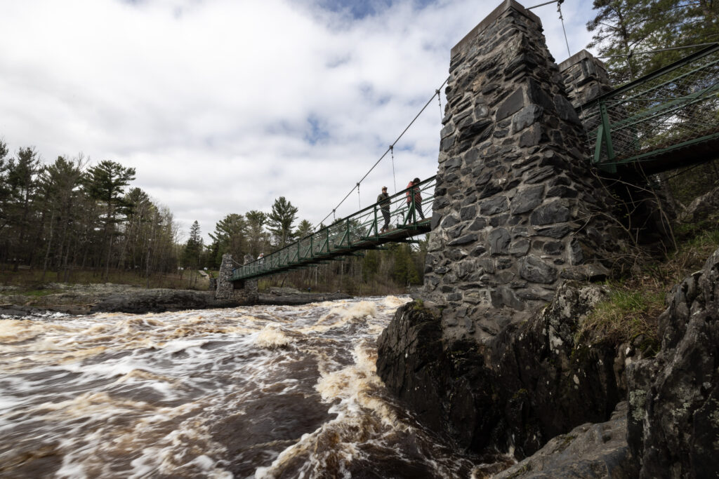 From a low angle, we can see a stone bridge with people walking across on top of a rushing river.