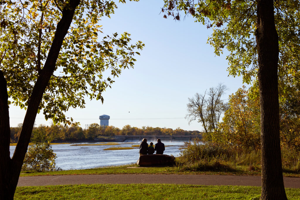 The silhouette of a family as they sit in the grass looking out at the river.
