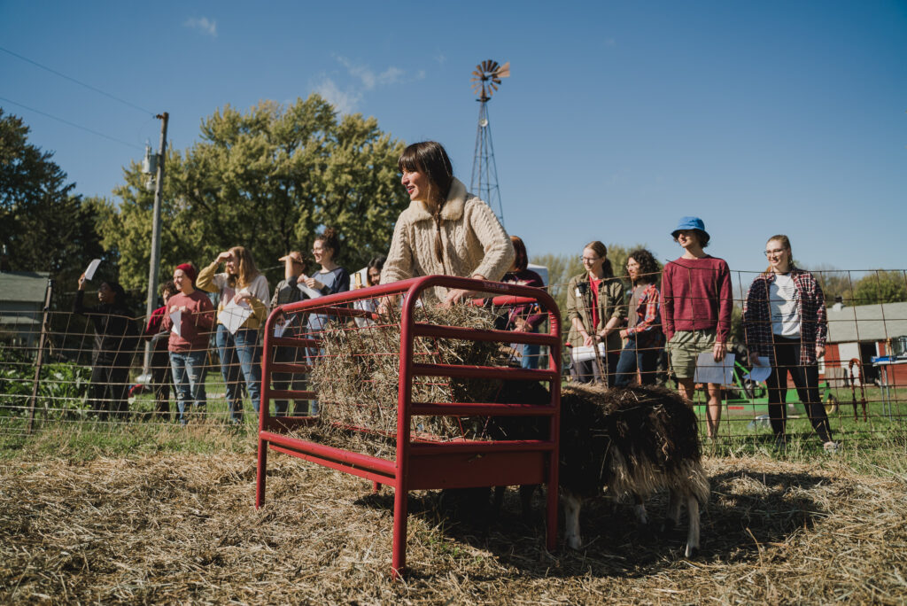 A woman stands near a cage of hay for feeding while a group of people look on.