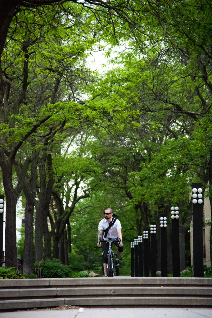 A man in a white shirt riding his bicycle toward the camera on the Loring Greenway.