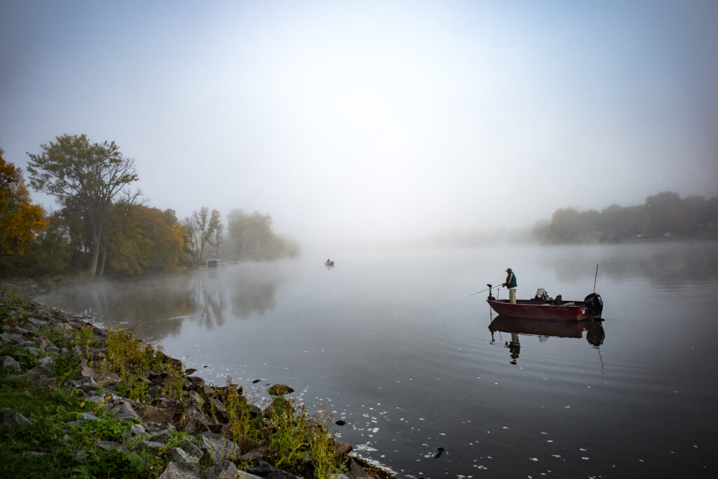 A silhouette of a person fishing on a foggy morning along a peaceful lake.