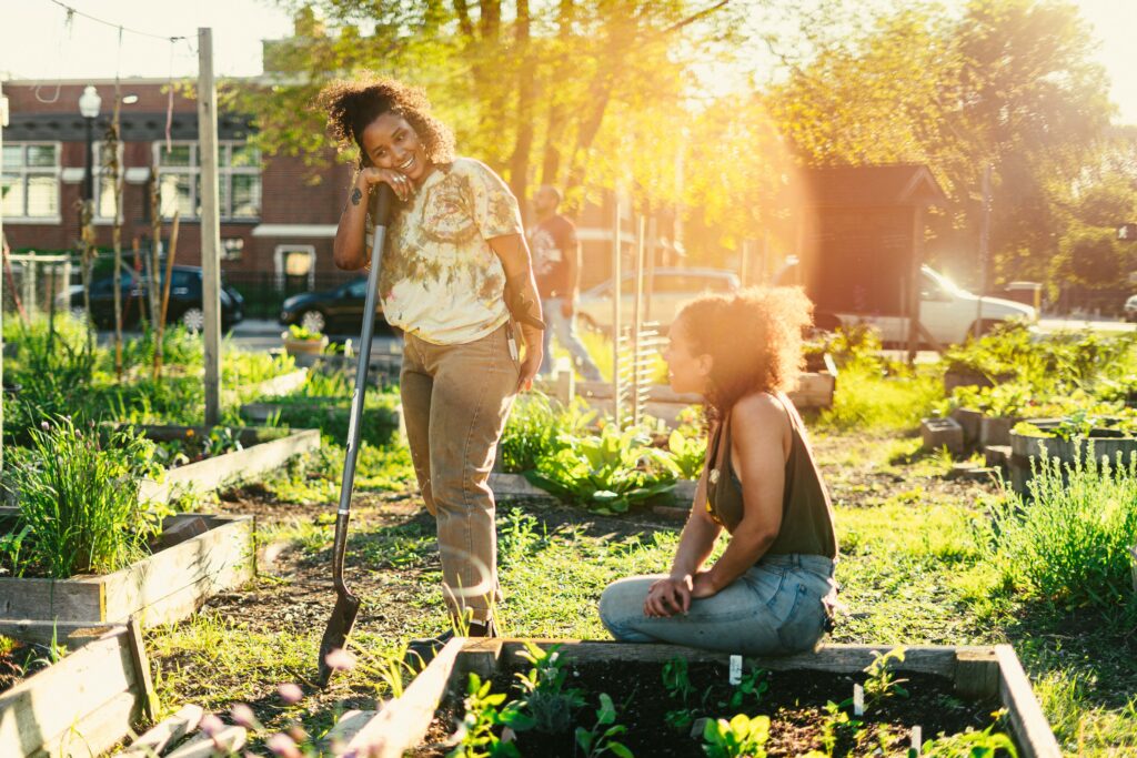 Two people, one leaning on a shovel and one kneeling by a garden plot, laugh during a break from work.