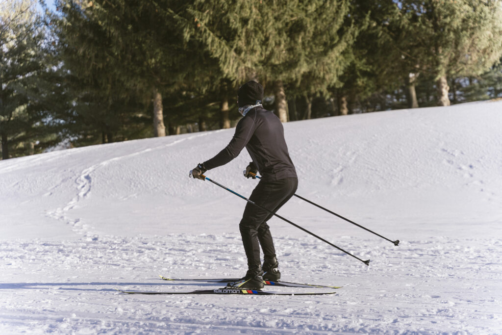 A person in all black jacket and tights cross country skiis away from the camera.