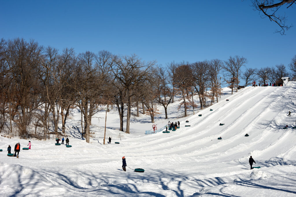 From a distance we can see a large sledding hill with children in tubs sliding down the many trails.