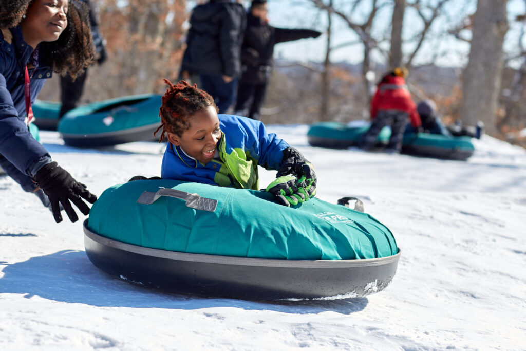 A young boy begins his descent down a sledding. hill on a blue intertube.