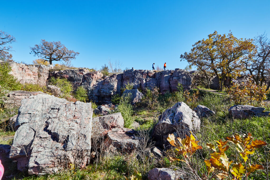 At the top of an outcropping of rocks you can see two people balancing at the top as grass grows up between the boulders.