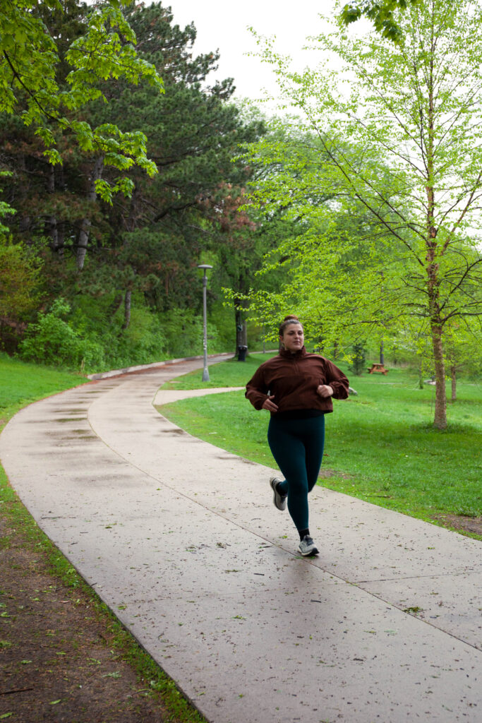 A woman in blue leggings and a red running jacket jogs down an asphalt path.